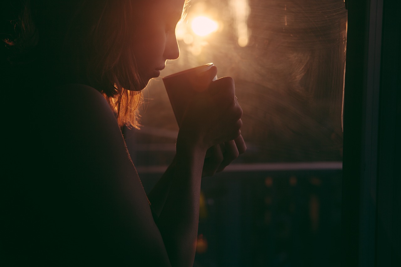 A woman holding a cup by a window in sunlight - Hannah Young Life Coaching